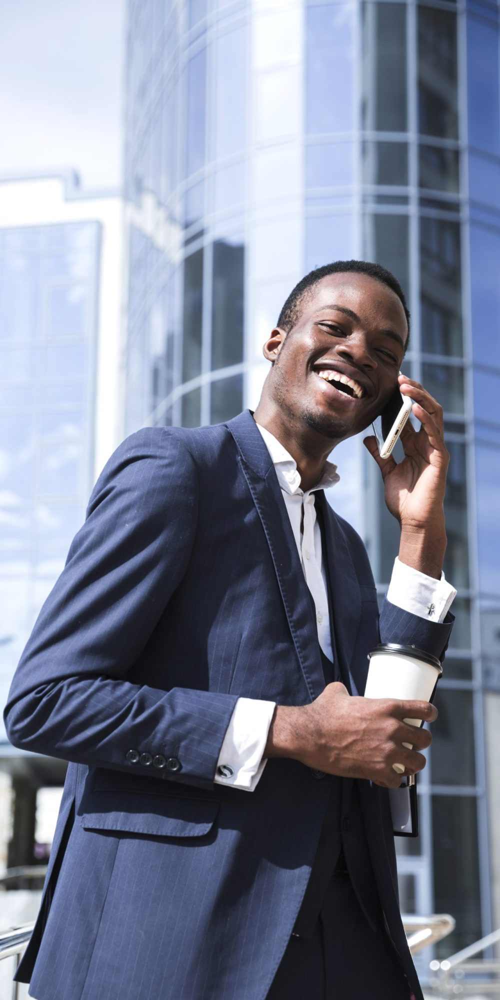 souriant-africain-jeune-homme-d-affaires-devant-le-batiment-de-l-entreprise-parler-sur-telephone-mobile